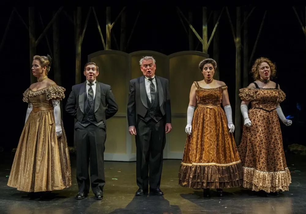 Two men in suits and three women in period dresses sing on a stage.